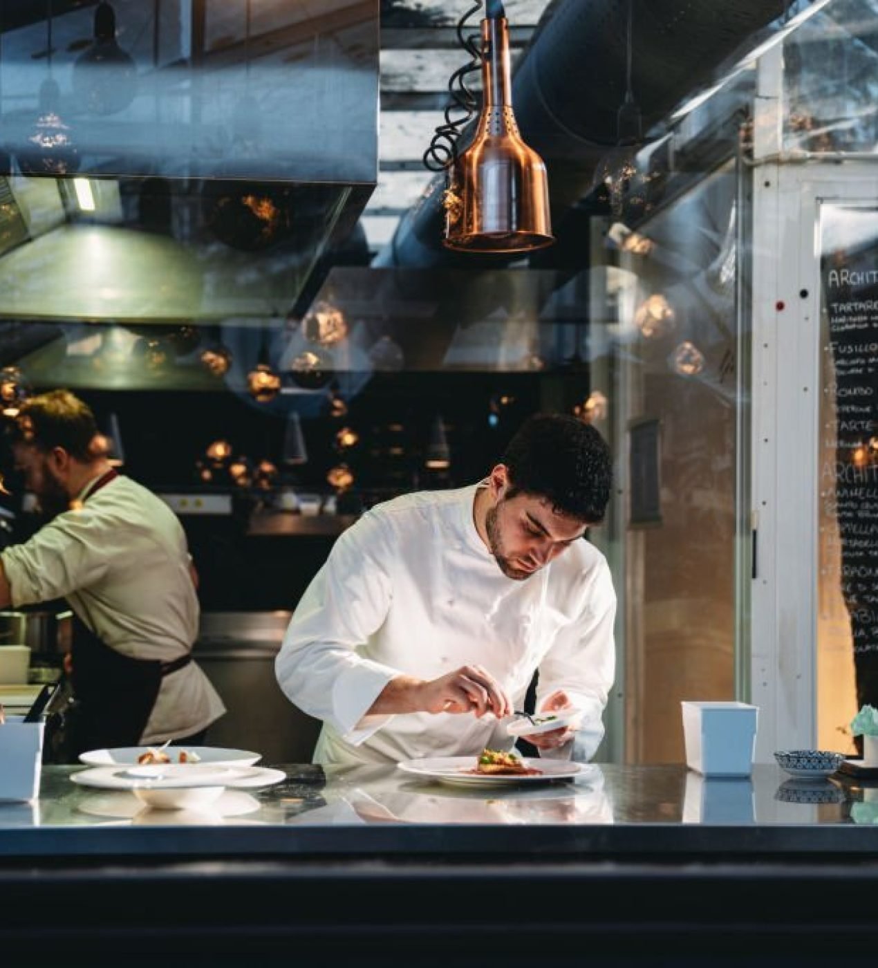 A chef is cooking in his restaurant's kitchen. Shot through the glass. High-end gourmet restaurant.